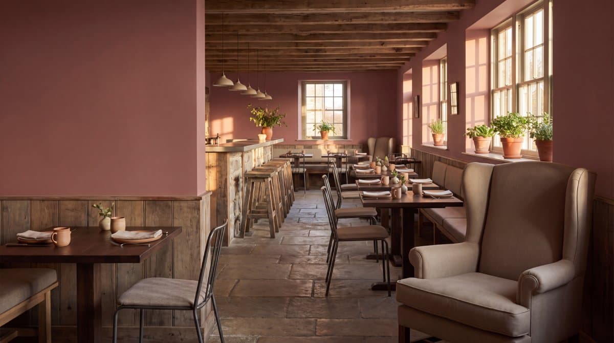 A restaurant dining room with rose walls, timber beams, stone floors and linen wingback chairs