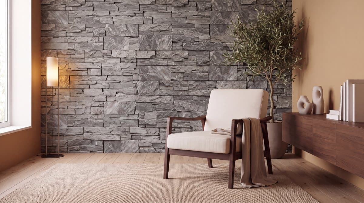 A grey stacked-stone feature wall behind a walnut lounge chair, a floor lamp and an olive tree